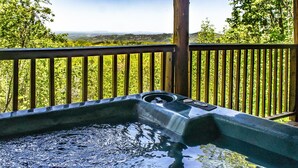Een hottub met een houten terras en een mooi uitzicht op heuvels en bomen.
