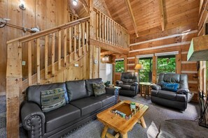 A log cabin interior with a wooden staircase, leather sofas, and a fireplace.