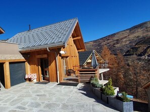A wooden cabin with a stone patio, a covered outdoor seating area, and a view of the surrounding hills. - Chalet, balcony, fireplace or stove, parking, ski locker, 150m², Valloire (Valloire)