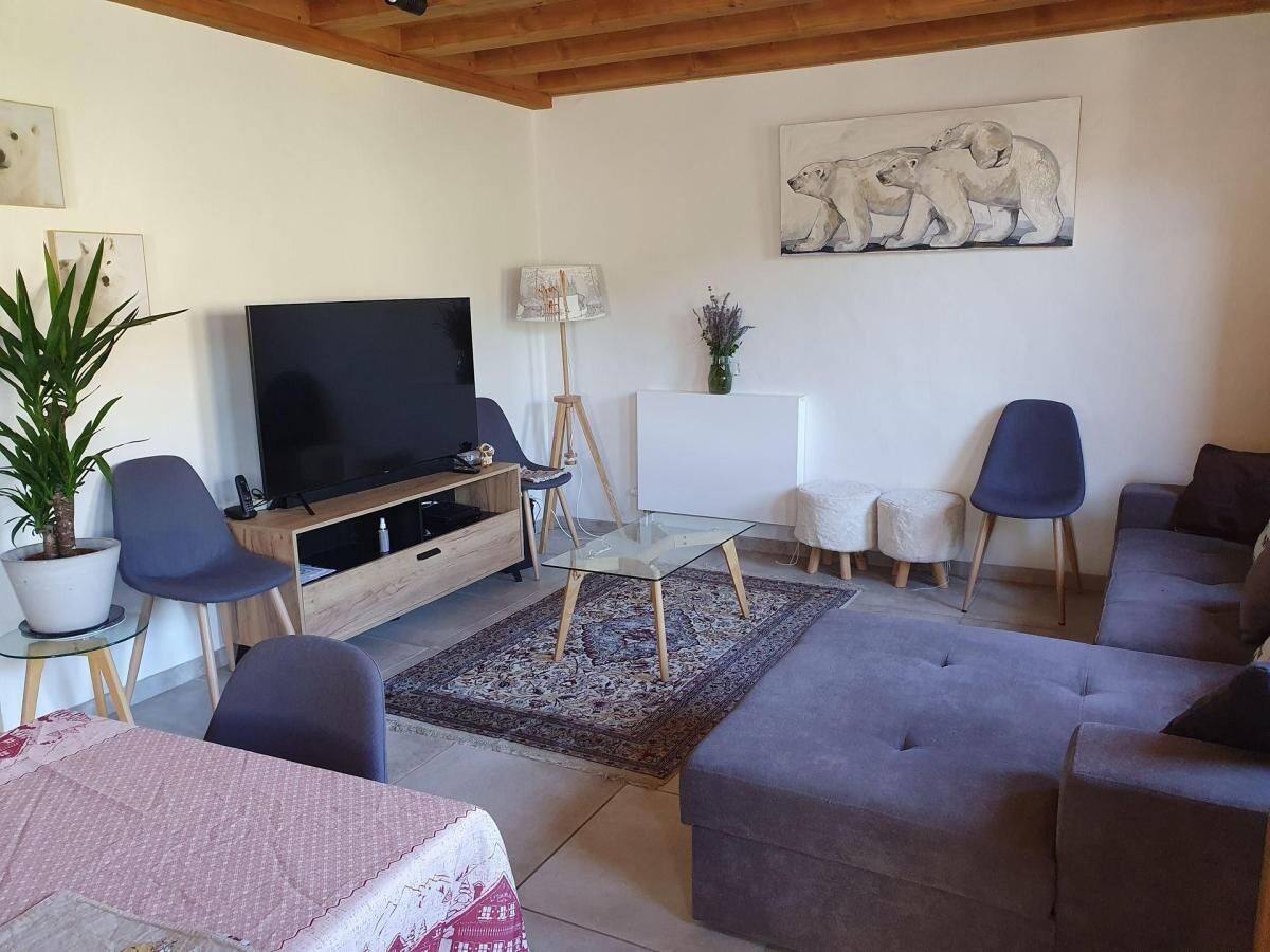 A living room with a flat-screen TV, a glass coffee table, a sofa, and a dining table with chairs.