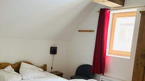A bedroom with a wooden bed, a red curtain, a radiator, and a window with a view. - 250m from ski slopes, 1st floor, terrace, parking, ski locker, 60m², Valloire (Valloire)