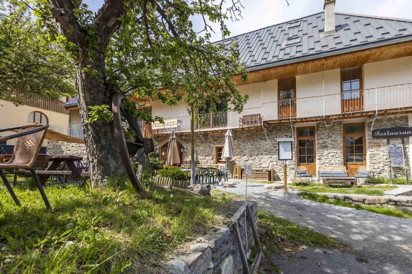 Ein Steinhaus mit einem Restaurantschild, Außenbestuhlung und einem Baum im Vordergrund.