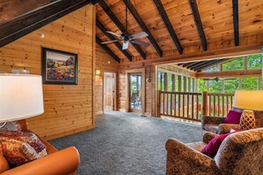 A log cabin interior with a ceiling fan, a painting, and a view of the outdoors. - Amazing Views w/ Theater & Game Room (Sevierville)