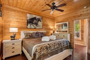A wooden-paneled bedroom with a bed, nightstands, a ceiling fan, and artwork.