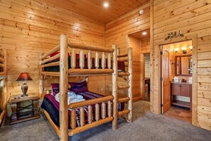 A wooden cabin room with a bunk bed, a small table with a lamp, and a door leading to a bathroom. - Amazing Views w/ Theater & Game Room (Sevierville)