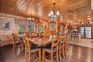 A wooden cabin interior with a dining area, kitchen, and large windows. - Amazing Views w/ Theater & Game Room (Sevierville)
