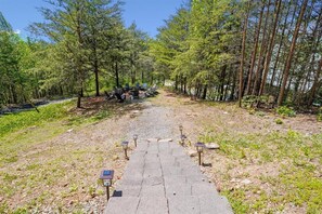 A paved path leading through a forested area with chairs and tables set up for outdoor dining.