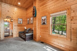 Ein gemütliches Blockhaus-Interieur mit Holzwänden, einer Couch, einem Fenster mit Blick auf den Wald und gerahmten Tierbildern.