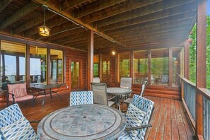A covered outdoor area with wooden flooring, metal-framed tables and chairs, and large windows. - Amazing Views w/ Theater & Game Room (Sevierville)