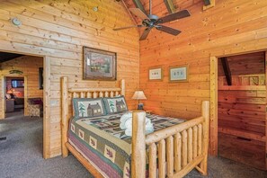Ein Holzblock-Interieur mit einem Bett, einem Deckenventilator und gerahmten Bildern an den Wänden.