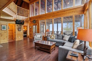 A spacious living area with a wooden floor, a sofa set, a coffee table, and a television mounted on the wall. - Amazing Views w/ Theater & Game Room (Sevierville)