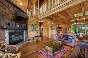 Interno di una baita di legno con camino, pavimento in legno, un divano e un'area da pranzo.