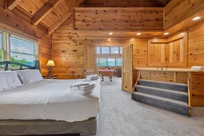 A log cabin bedroom with a bed, a bathroom with a tub, and a staircase. - Romantic Log Cabin w/ Hot Tub & Views (Sevierville)