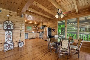A wooden cabin interior with a dining area, kitchen, and large windows.