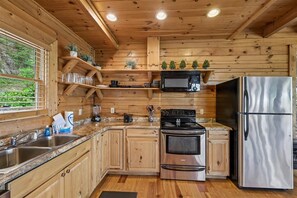 Cucina di una baita in legno con piani di lavoro in granito, elettrodomestici in acciaio inossidabile ed scaffali a muro.