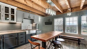 A modern kitchen with wooden beams, grey cabinets, a large island, and bar stools.