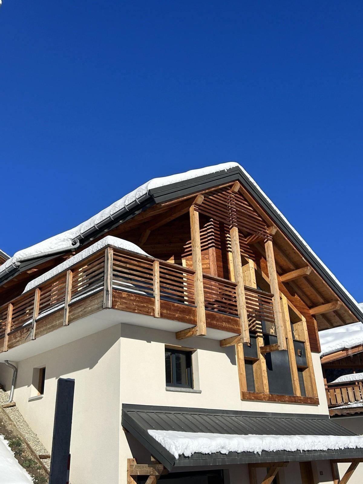 Un chalet en bois à deux étages, doté d’un balcon, avec de la neige sur le toit et un ciel bleu dégagé.