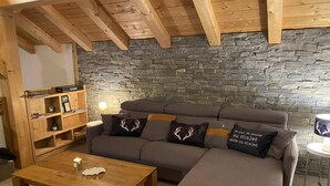 Una sala de estar acogedora con pared de piedra, vigas de madera, un sofá, una mesa de centro y una estantería.