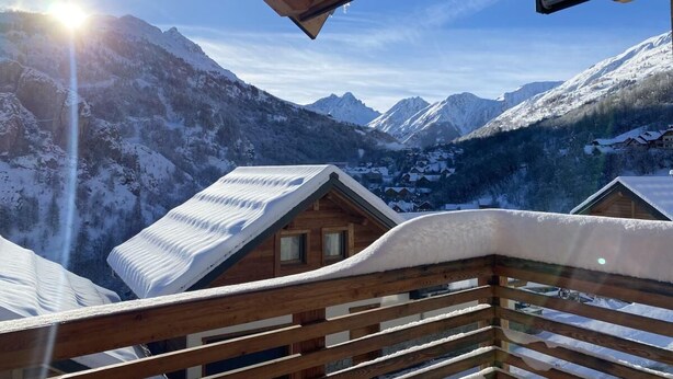 Un balcón de madera con vistas a montañas nevadas y una casa al fondo.
