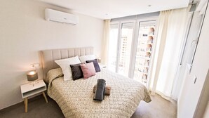 Ein Schlafzimmer mit einem Bett, Nachttischen, einer Klimaanlage und Blick auf ein Gebäude durch das Fenster.