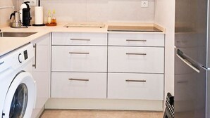 Eine moderne Küche mit weißen Schränken, einer eingebauten Mikrowelle, einem Edelstahlkühlschrank und einer Waschmaschine.