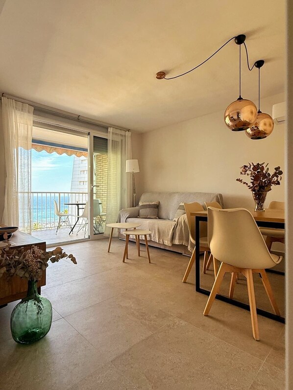Sala moderna com sofá, mesa de jantar e cadeiras. Possui varanda com vista para o mar.