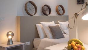 A neatly arranged hotel room with a bed, bedside lamp, wall-mounted decorative items, and a fruit bowl on the nightstand.
