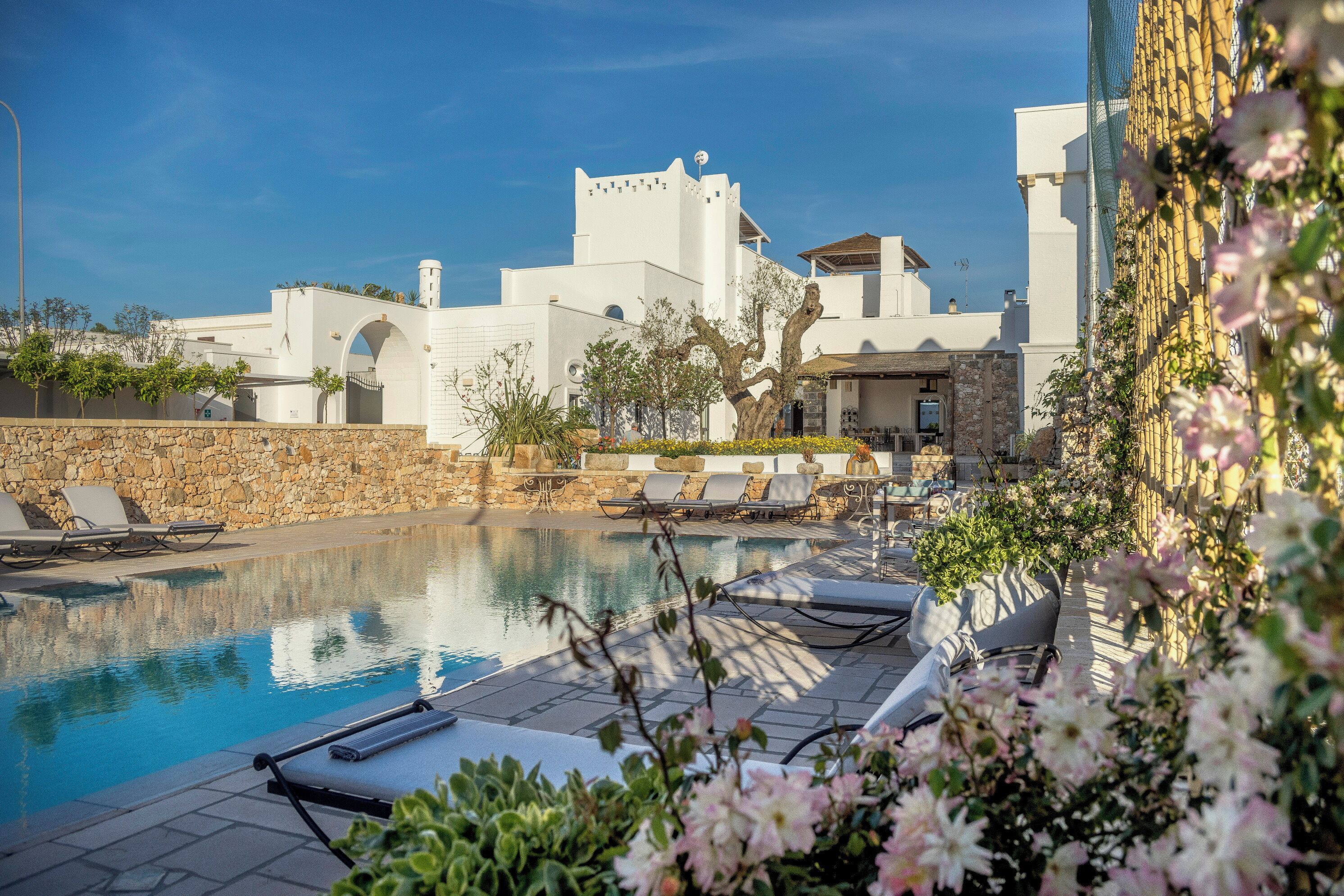 Un área de piscina con sillones de descanso, un muro de piedra y un edificio de arquitectura blanca.