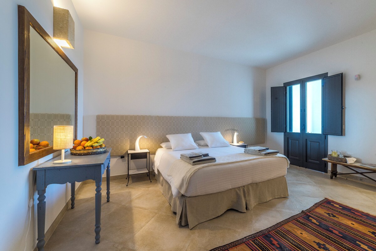 Un dormitorio con cama, mesitas de noche, un espejo y una cesta de fruta.