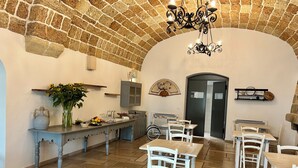 A rustic dining area with stone walls, a chandelier, and white wooden furniture.