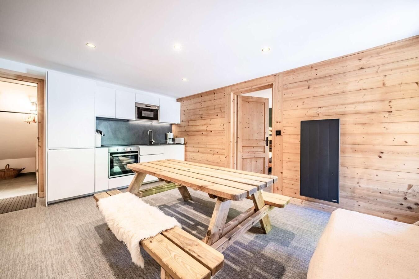 Une cuisine moderne avec des meubles blancs, une table à manger en bois et des bancs.