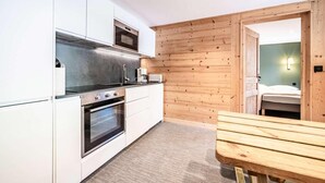 A compact kitchen with white cabinets, a built-in oven, and a microwave. There's a wooden table and a bench in the dining area. - 200m from ski lifts, Ground floor, terrace, parking, tv, 45m², Morzine (Morzine)