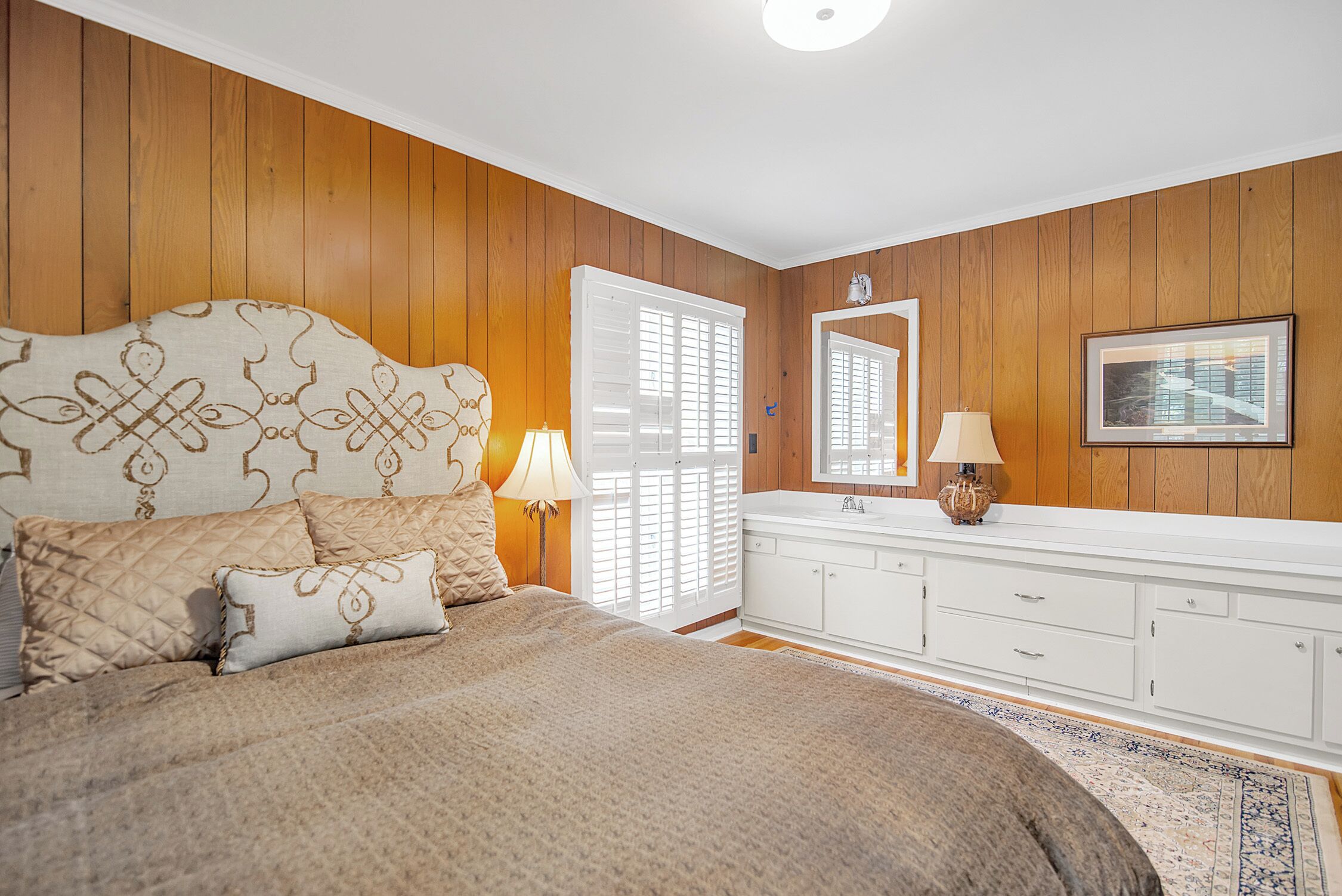 A bedroom with a large bed, a white dresser, a mirror, and a framed picture on the wall.