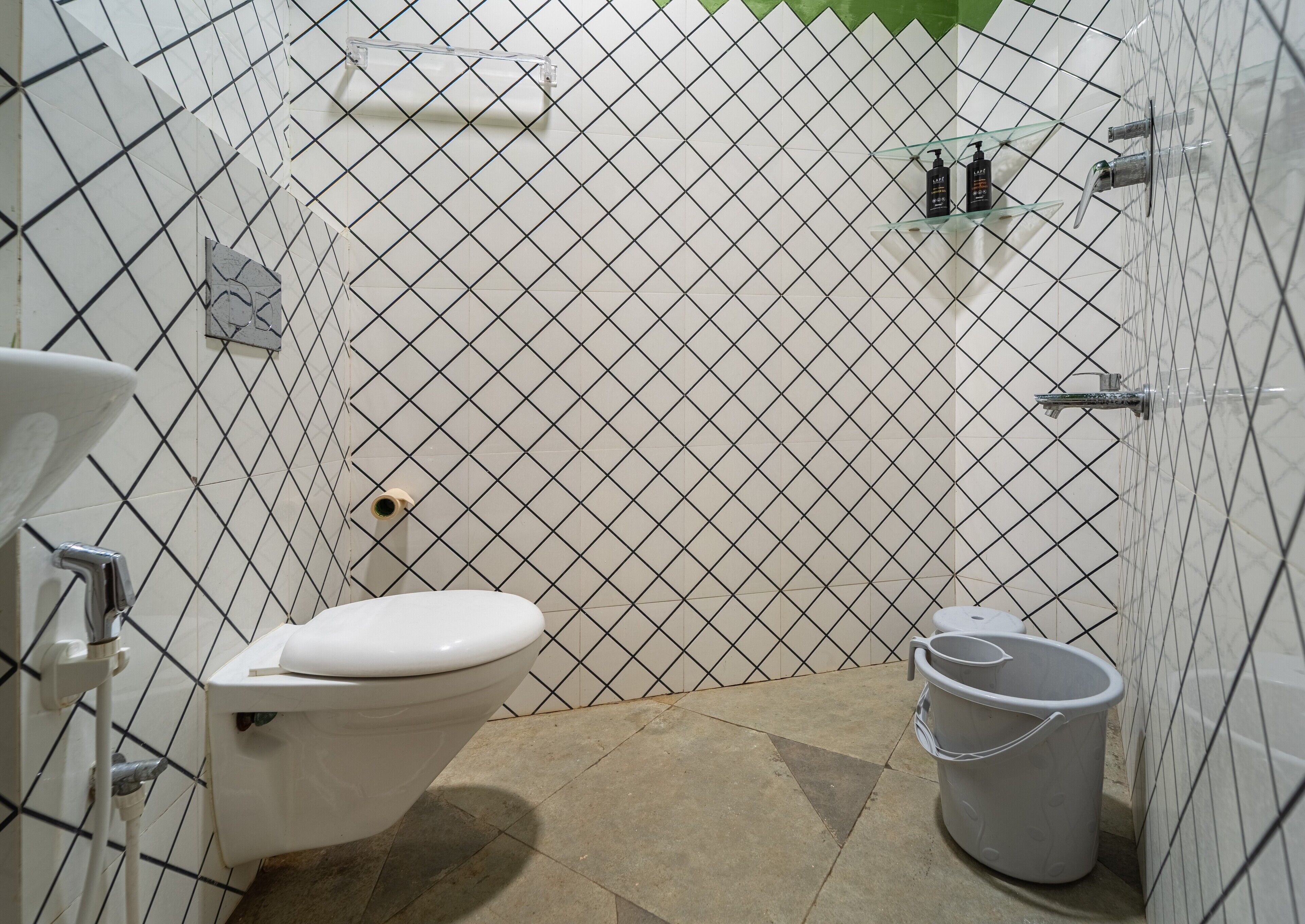 Un baño con un inodoro blanco, un bidé, un pequeño estante con artículos de aseo y un cubo.