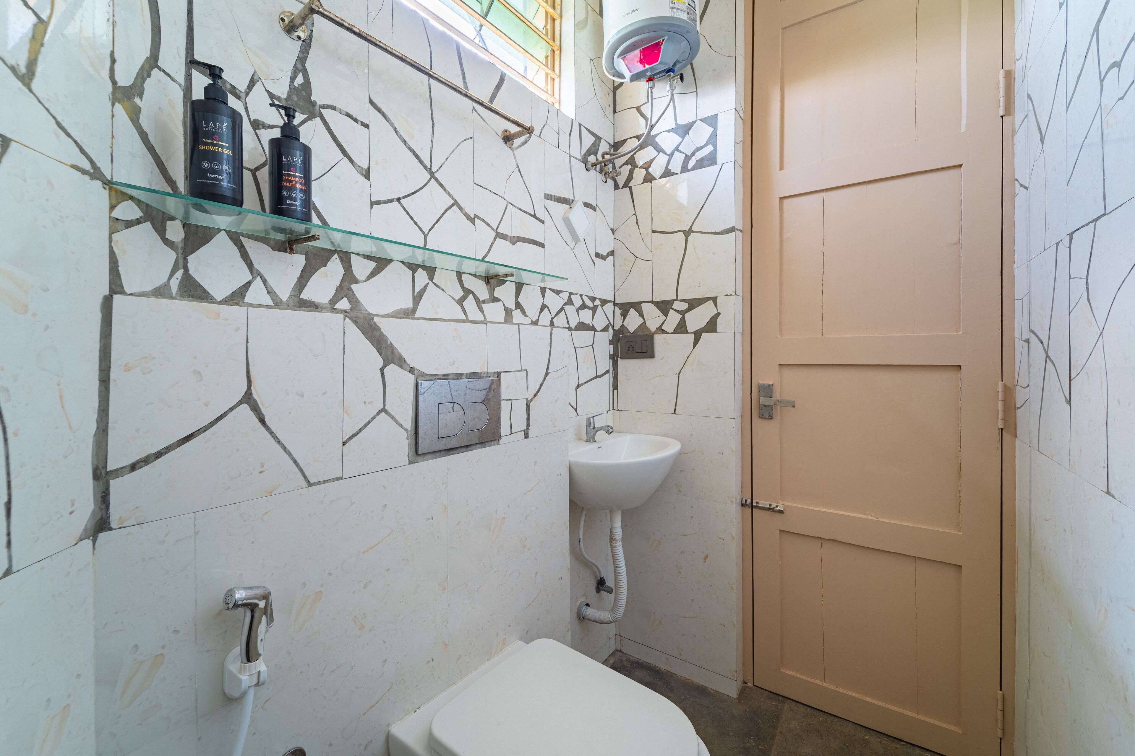 Une salle de bain avec des toilettes blanches, une étagère en verre contenant des articles de toilette, un lavabo blanc et une porte.