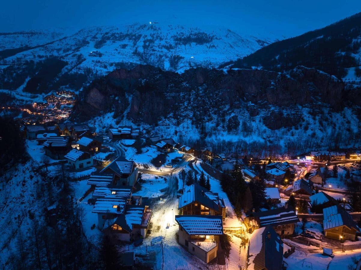 Ein schneebedecktes Dorf bei Nacht mit beleuchteten Gebäuden und einer kurvenreichen Straße.