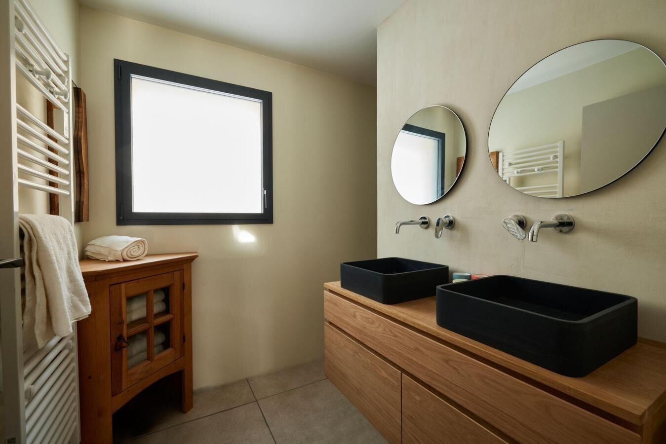 Une salle de bain moderne avec un meuble-lavabo en bois, deux vasques noires et deux miroirs ronds.