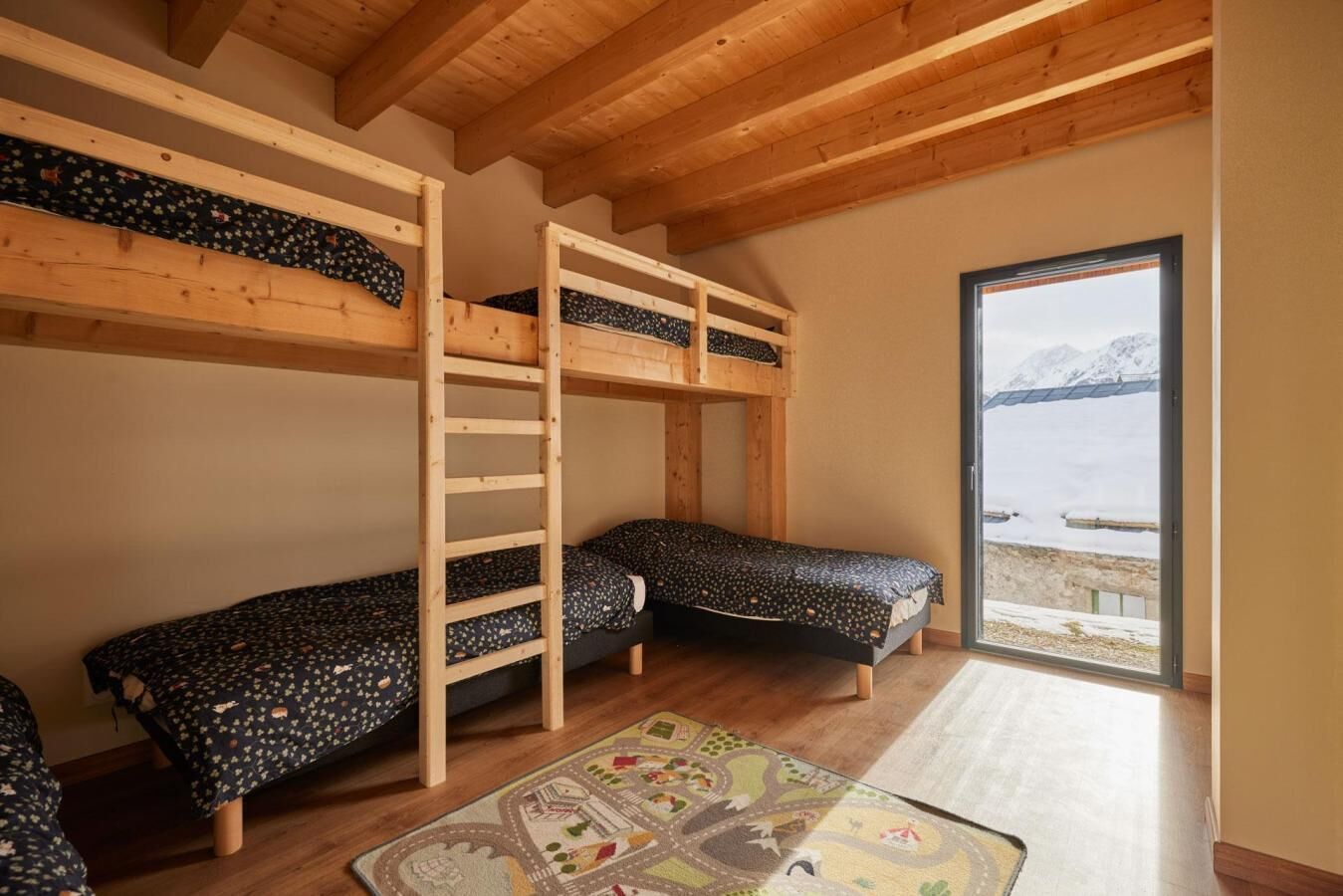 A room with bunk beds, a large window with a view of a snowy landscape, and a colorful rug on the floor.