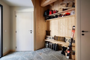 Ein Skiraum mit Regalen für Ski und Stiefel, eine Bank mit Kissen und eine Tür zu einem weiteren Raum.
