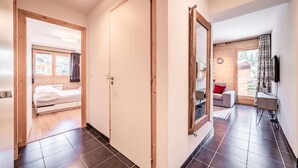 Ein modernes Hotelzimmer mit Holztür, einem Bett, einem großen Spiegel und Blick auf einen Balkon mit Sofa und Fernseher.