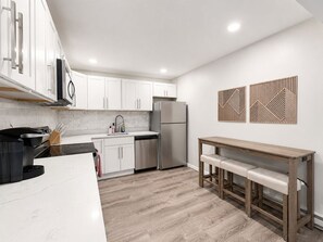 A modern kitchen with white cabinets, stainless steel appliances, a wooden bench, and decorative wall art.