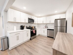 A modern kitchen with white cabinets, stainless steel appliances, and a wooden floor.