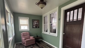 A hallway with a wooden floor, a pink chair, a potted plant, a wall-mounted light fixture, and a door with a window. - Red Roof Retreat - cozy home in Carson (Carson)