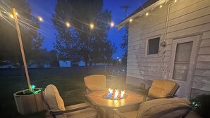An outdoor patio with a fire pit, two chairs, and string lights. - Red Roof Retreat - cozy home in Carson (Carson)