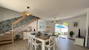 A modern dining area with a wooden staircase, a dining table set for four, and a view of the outdoors through a glass door. - Rincon del Mar - House with spa and hammocks, just 8 minutes from the sea (Saint-Hilaire-de-Riez)