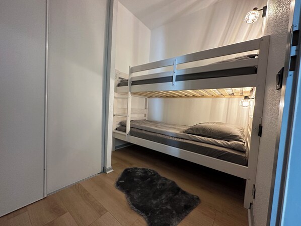 A bunk bed with a light fixture above it, a dark rug on the floor, and a white door on the left.