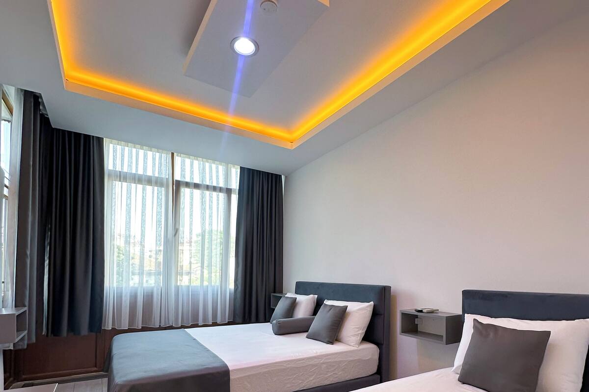 A hotel room with two beds, a ceiling light, and a window with curtains.
