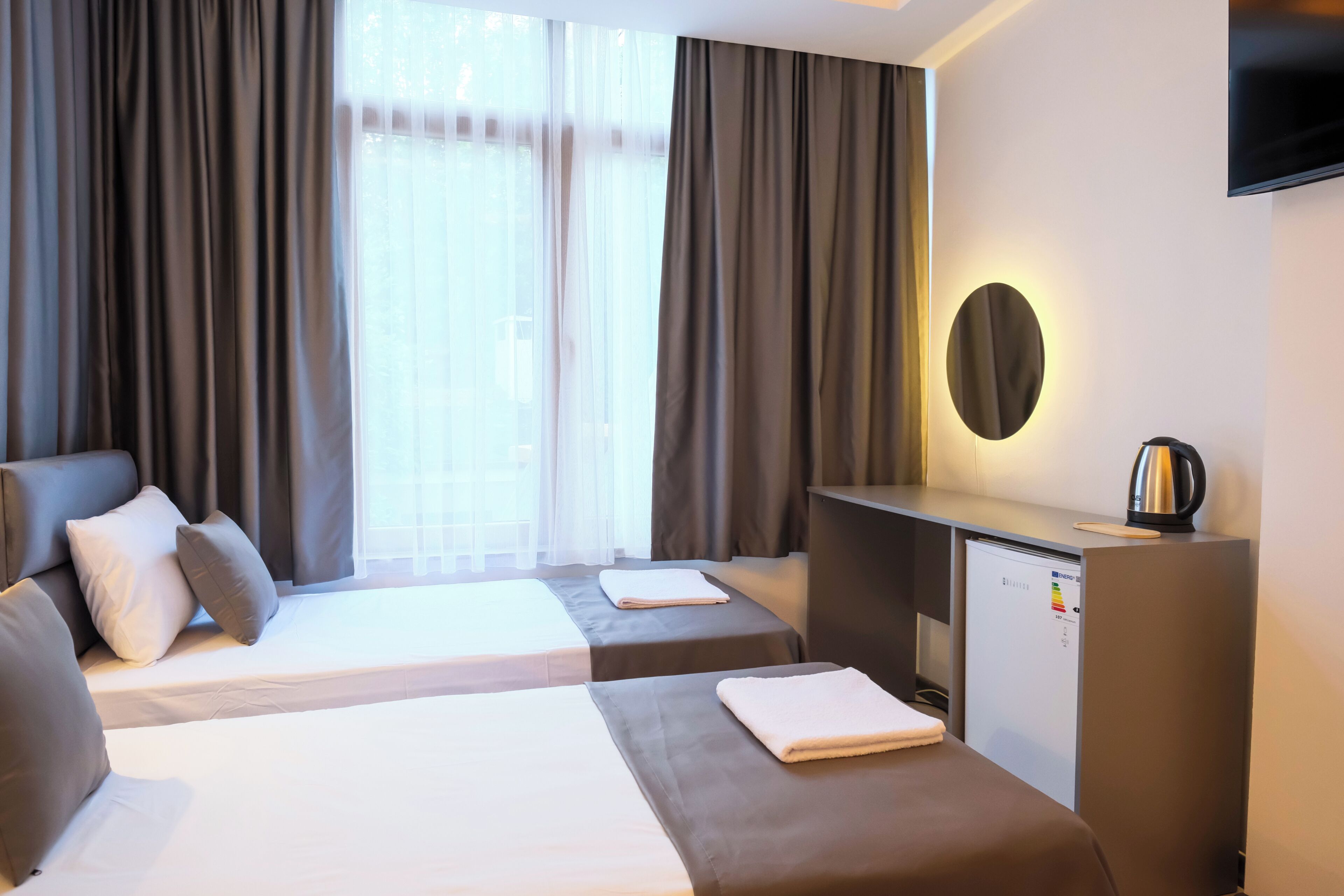 A hotel room with two beds, a desk, a television, and a refrigerator.