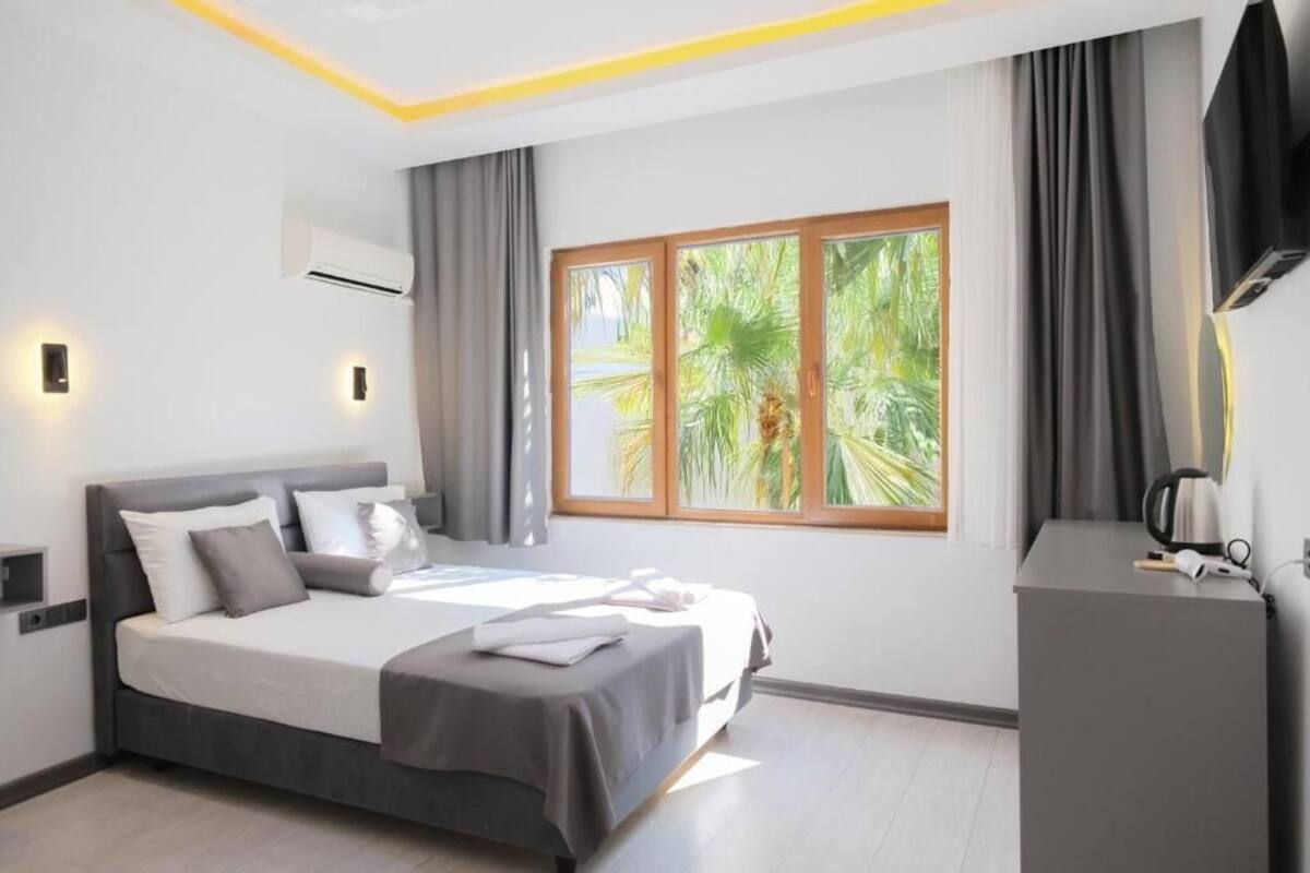A modern hotel room with a large bed, a desk, and a window with a view of greenery.