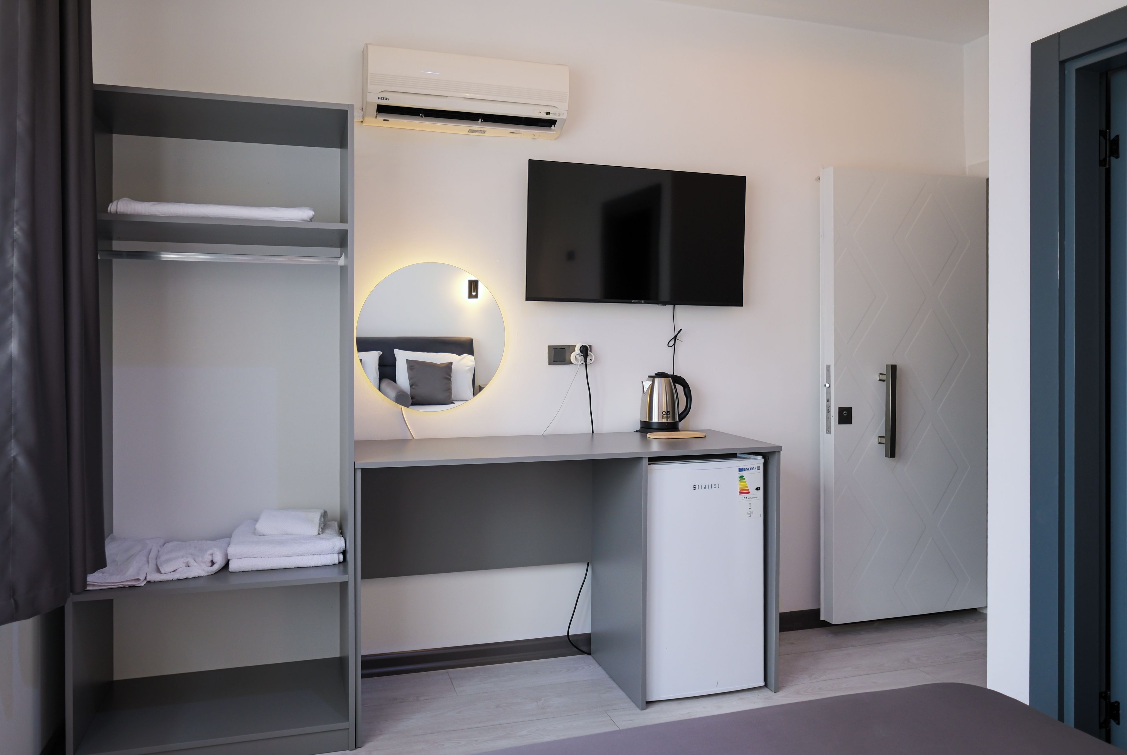 Een moderne hotelkamer met een bed, een bureau met een flatscreen televisie, een minibar en een ingebouwde airconditioning.